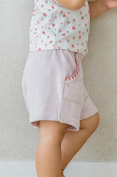 Toddler wearing Avauma Pocket Day Shorts in Milk Pink, standing against a wall in soft natural light